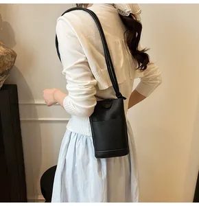 Detail of black litchi grain leather bucket bag worn as a crossbody with thin strap