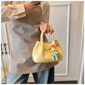 Close-up of yellow pleated bucket bag with doll charm and decorative strap buckle