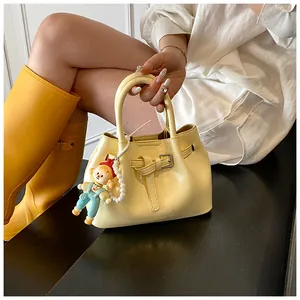 Detail of light yellow bucket bag featuring decorative belt and cartoon pearl charm