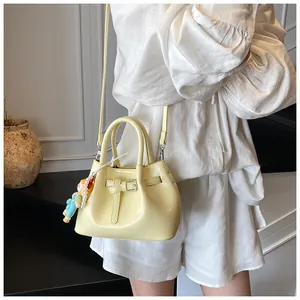Detail of cream yellow pleated bucket bag with pearl doll charm and slim shoulder strap