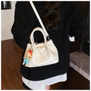Close-up of beige pleated bucket bag with metal ring handles and cartoon charm accessory