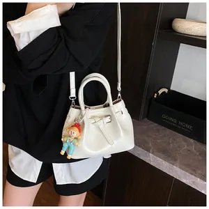 Close-up of cream pleated bucket bag with doll pendant and adjustable shoulder strap
