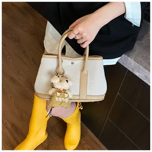 Detail of canvas tote bag with leather trim and cute brown teddy bear plush charm