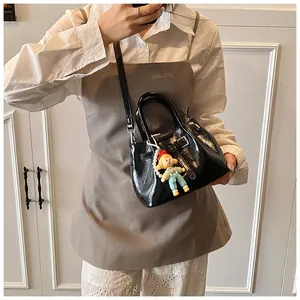 Detail of black glossy bucket bag with detachable strap and cute doll pendant