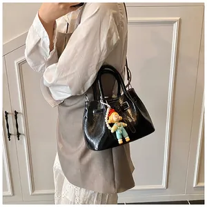 Detailed view of black patent leather bucket bag with cute doll charm pendant