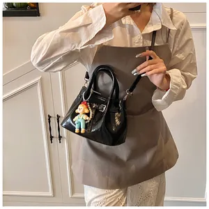 Detail of glossy black bucket bag with buckle and cute doll charm on a model