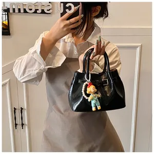 Close-up of black glossy pleated bucket bag with pearl chain doll pendant and buckle detail