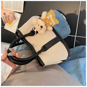Canvas tote bag detail with black leather trim and a cute plush bear charm accessory