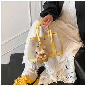 Detail of yellow and beige contrast tote bag featuring a cute teddy bear charm