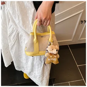 Detail of yellow leather and beige canvas tote bag with a cute teddy bear charm