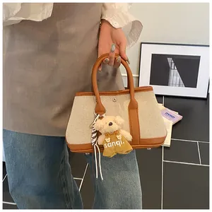 Detail of off-white canvas tote with brown leather handles and a plush bear pendant