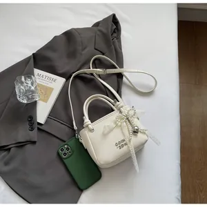 Détail du mini sac seau en cuir crème avec nœud en perles et lettrage métallique
