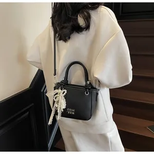 Détail du mini sac seau noir en cuir grainé avec nœud en dentelle et breloque perle