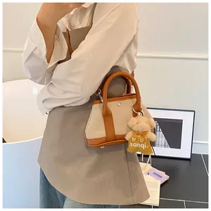 Detail view of canvas and leather mini tote bag with a cute brown plush bear charm