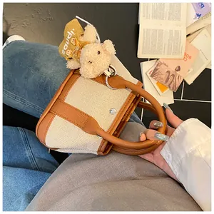 Detail of canvas tote bag with brown leather trim and a cute plush bear charm