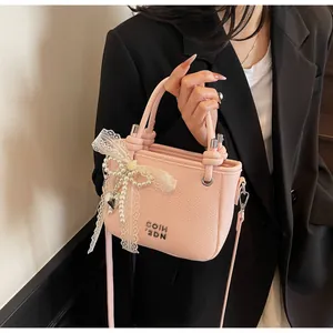 Détail d'un sac seau rose grainé avec nœud en dentelle perlé et pendentif coeur