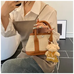 Detail of canvas tote bag with brown leather trim and a cute teddy bear plush charm