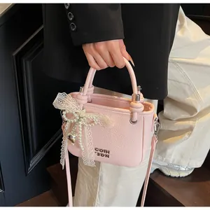 Détail du sac seau rose en cuir grainé avec nœud en dentelle et breloque perle