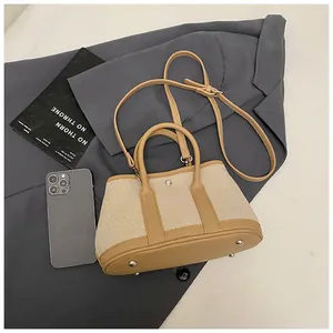 Detail of canvas tote bag showing metal base studs, leather handles, and shoulder strap