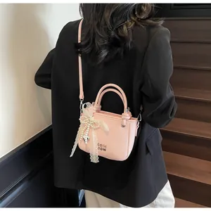 Sac seau rose à texture litchi avec breloque nœud en perles porté en bandoulière chic