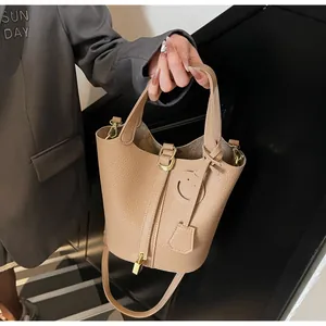 Detail of khaki pebbled leather bucket bag with gold lock and smiley charm on model
