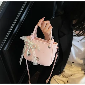 Détail du sac seau rose en cuir grainé avec nœud en dentelle et breloque cœur en métal