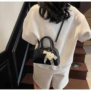 Dettaglio mini borsa nera in pelle a grana con fiocco di perle e tracolla regolabile