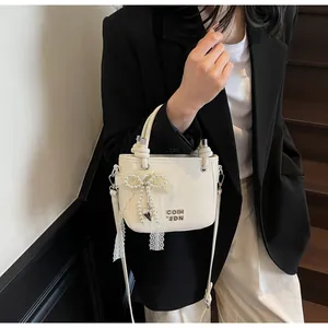Détail du sac seau en cuir crème avec breloque perles et nœud en dentelle élégant