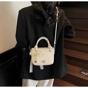 Vue détaillée du sac seau crème avec texture litchi, nœud en dentelle et pendentif perle