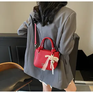 Détail du sac seau en cuir grainé rouge avec nœud en dentelle et breloque perle en cœur