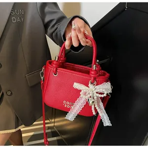 Détail du sac seau en cuir rouge avec nœud en dentelle, perles et breloque cœur