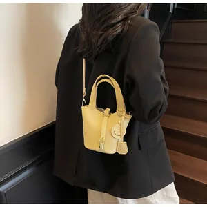 Detail of light yellow leather bucket bag with top handles and smiley face charm