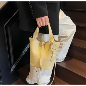 Detail of cream pebbled leather bucket bag with golden padlock and smiley face charm