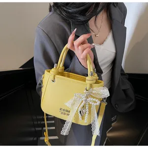 Détail du sac à main jaune en cuir grainé avec nœud en dentelle perlée et logo en métal
