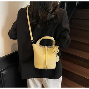Rear view of yellow PU bucket bag with smiley charm on model in black blazer