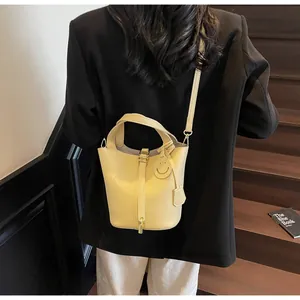 Detail of a creamy yellow lychee leather bucket bag with a smiley face charm and metal buckle
