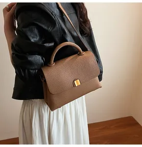 Détail d'un sac à bandoulière en cuir grainé marron avec fermoir métallique doré sur modèle