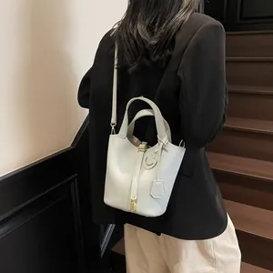 Light gray pebbled leather bucket bag with gold lock and detachable strap on model