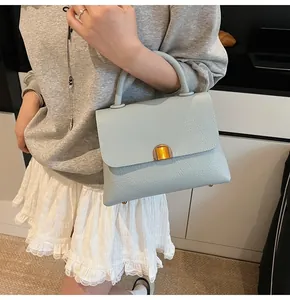 Sac à main bleu clair en cuir grainé avec fermoir doré porté par un mannequin