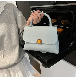 Détail d'un sac à main bleu clair en cuir grainé avec un fermoir métallique doré carré