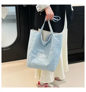Détail du sac cabas bleu clair avec texte beyou et merci porté avec une tenue chic
