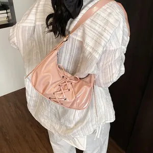 Pink glossy lace-up dumpling bag with stylish bow accent for women shown on shoulder