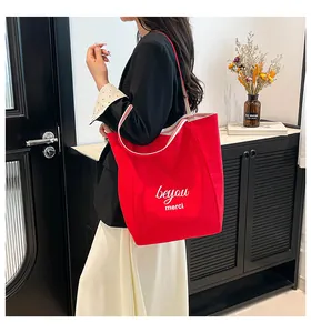 Détail d'un grand sac cabas en toile rouge avec des bandoulières rayées sur modèle