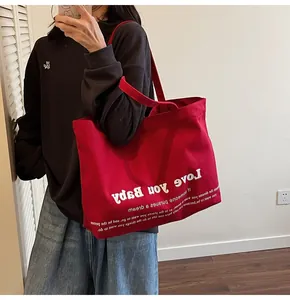Detail of red canvas tote bag with Love You Baby print worn on shoulder