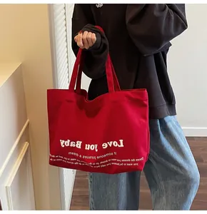 Detail of red canvas tote bag with Love You Baby print held by a model for daily use