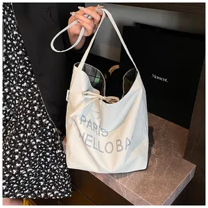 Detail of white canvas tote featuring green plaid lining and a bow tie closure
