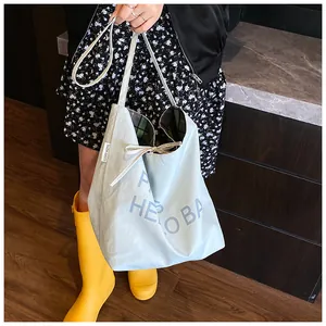 Detail of light blue canvas tote bag with bow tie closure and letter print on wood floor