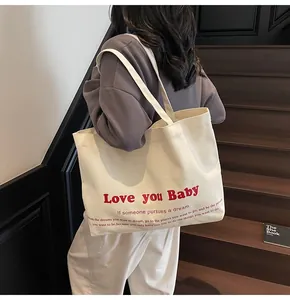 Close-up of beige canvas tote bag with red Love you Baby print worn on shoulder