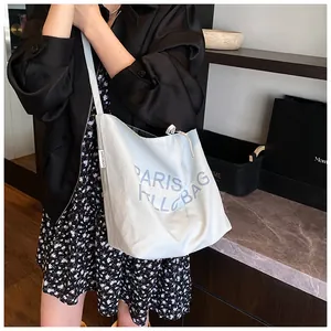 Detail of white canvas tote bag with blue Paris Hello Bag print worn by model