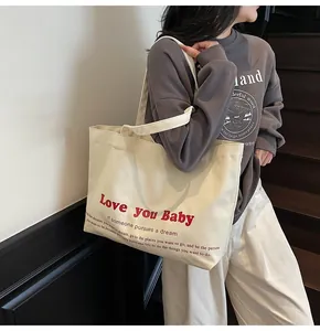 Detail of a large off-white canvas tote bag featuring a red Love you Baby slogan print